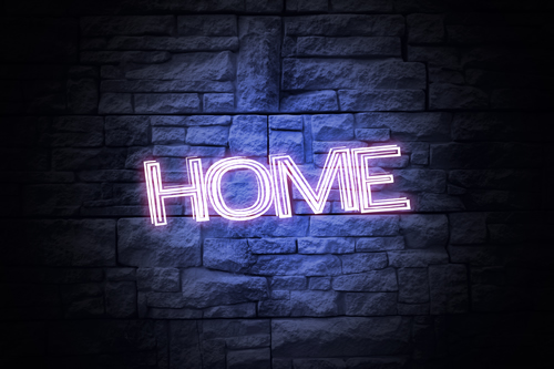 This is an image of a neon sign that says HOME and is glowing on top of a brick background.